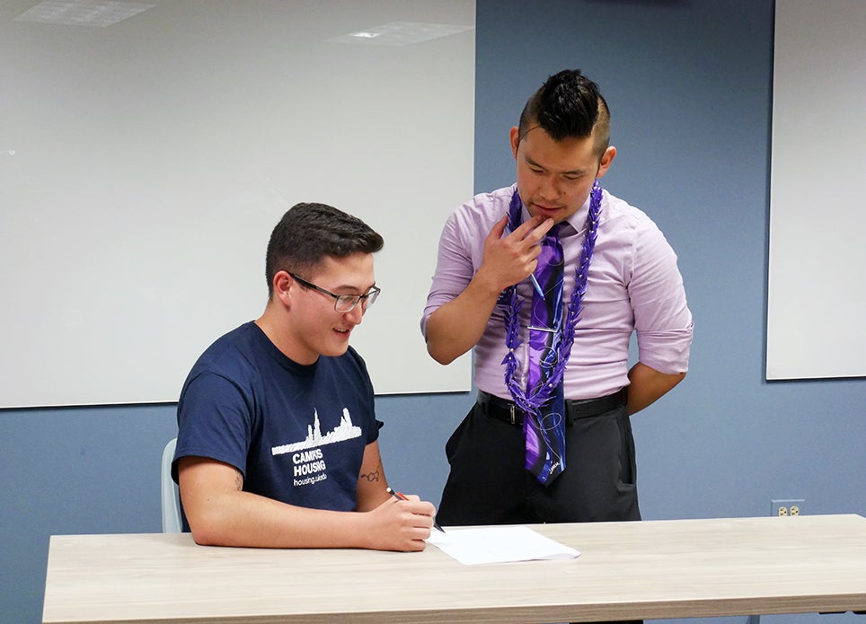 Fellow standing over a student as they write in a classroom