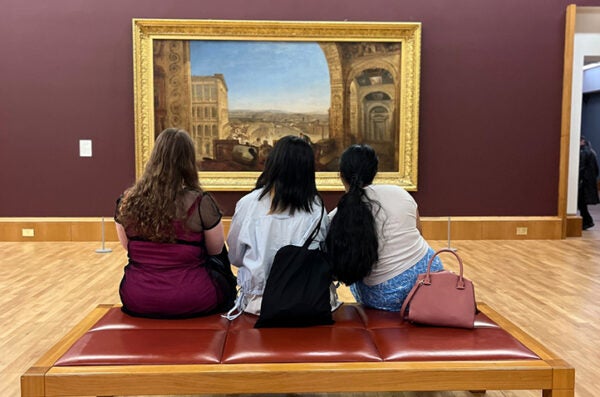 Students sitting on a bench looking at a painting.