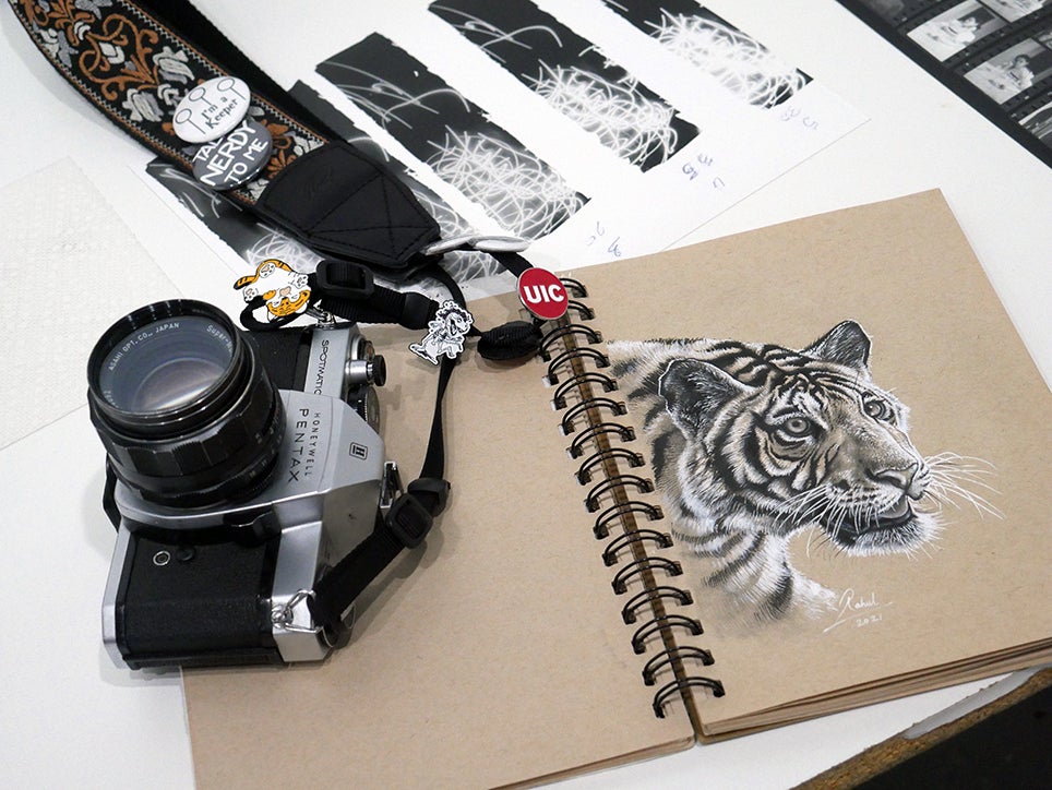 A camera on top of notebook with a drawing of a tiger.