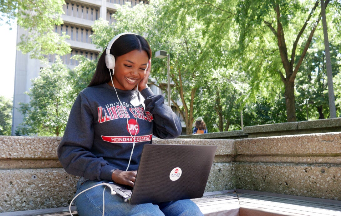 A student looking at their computer outside wearing UIC merch