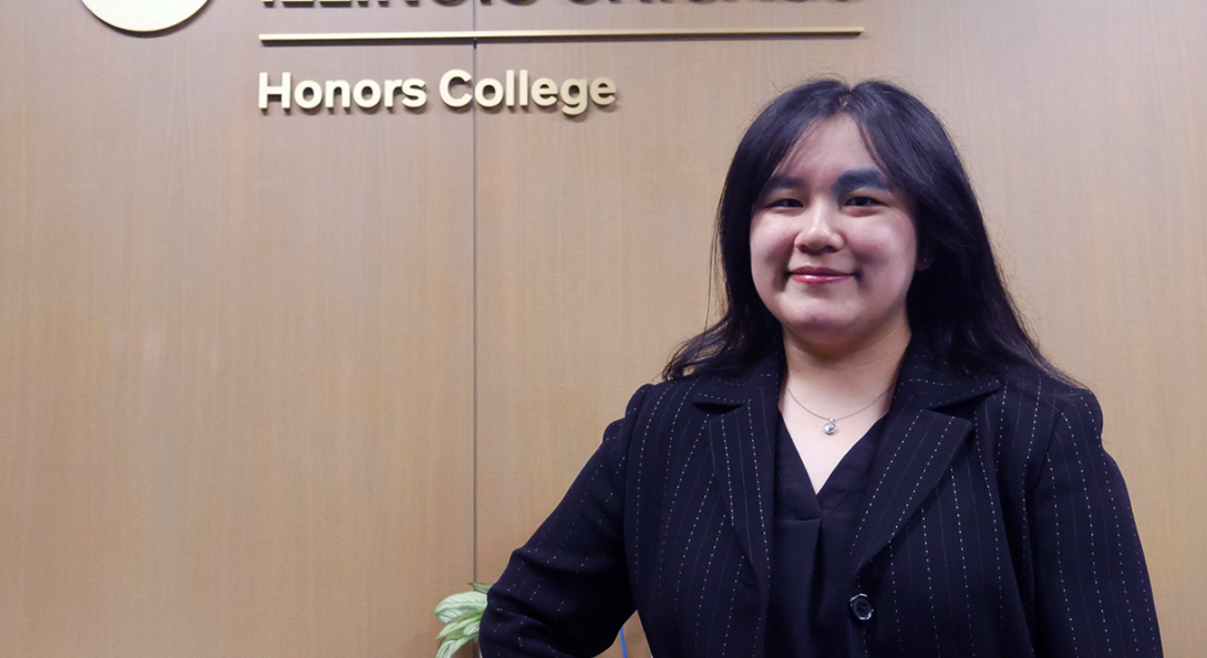 Student standing in front of UIC Honors College logo