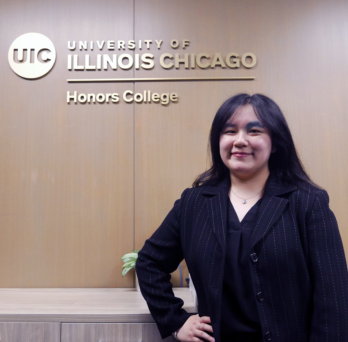 Student standing in front of UIC Honors College logo 